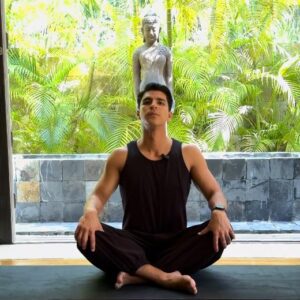 Mauricio from Livana Life demonstrating a seated forward fold yoga stretch to release neck and shoulder pain, sitting on a dark mat in a calm studio environment